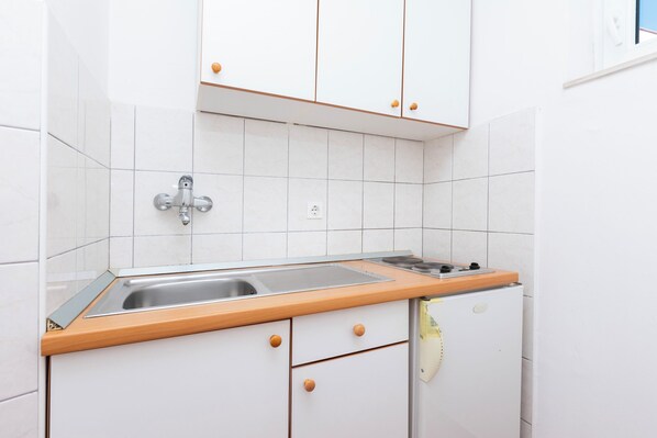 A kitchen with white cabinets, a wooden countertop, a sink, and a refrigerator. - Apartments Zoran (Podgora)