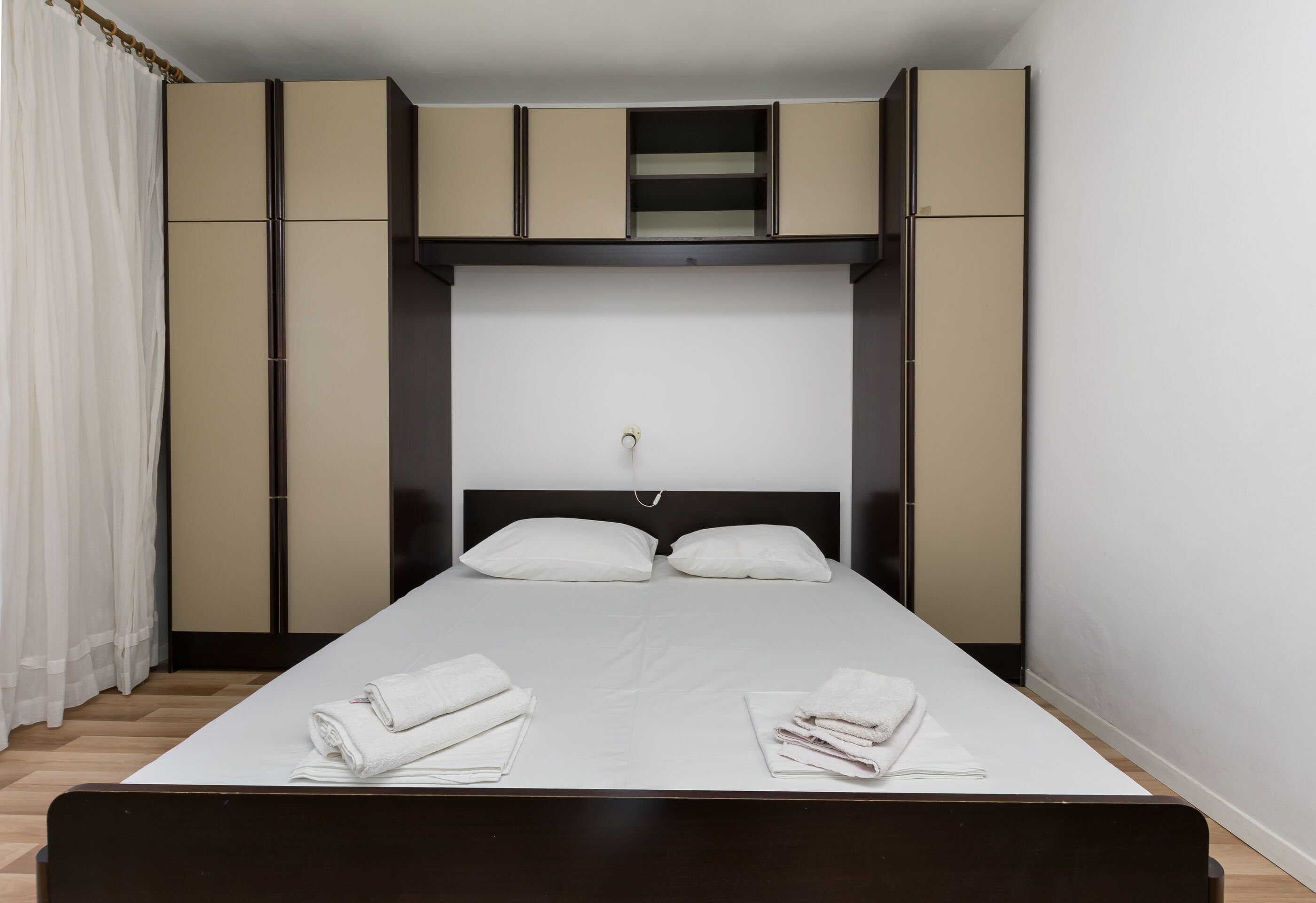 Ein ordentlich bezogenes Bett mit Kopfteil, einer kleinen Ablage darüber und einem weißen Handtuchpaar auf dem Bett.