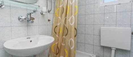 Une salle de bain avec un lavabo blanc, une étagère en verre, un rideau de douche à motifs circulaires et des toilettes.