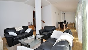 Ein modernes Wohnzimmer mit schwarzen Ledersofas, einem Glastisch und einer Treppe, die in einen Essbereich führt.