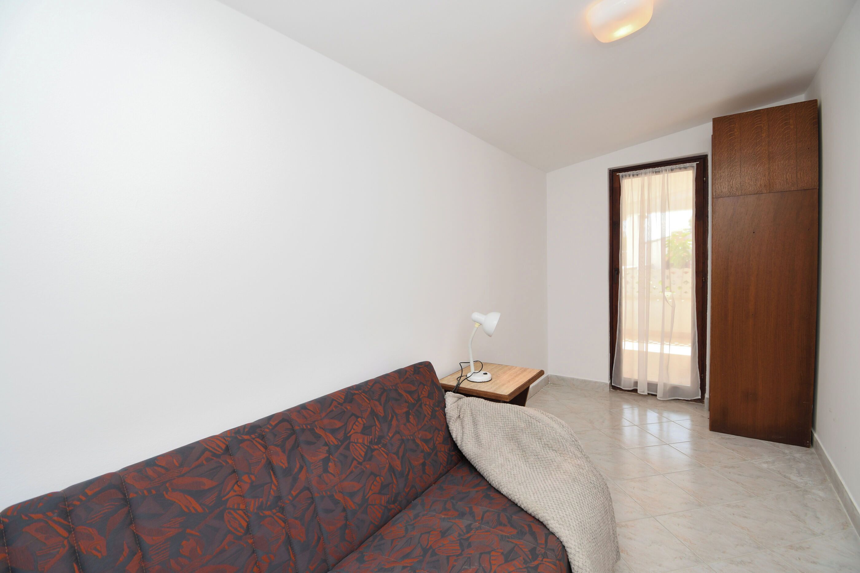 Un salon moderne avec un canapé à motifs, une petite table d’appoint en bois sur laquelle se trouve une lampe, et une porte coulissante donnant sur un espace extérieur.