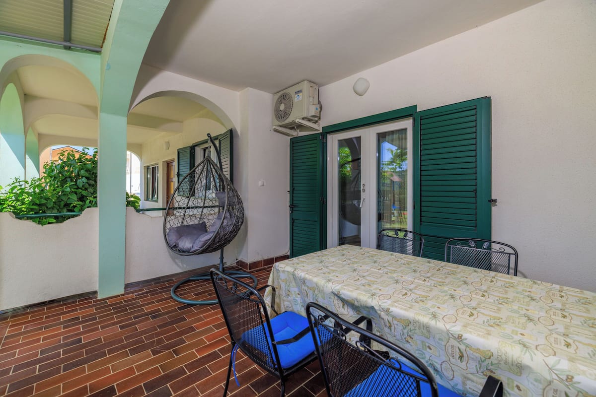 Un espace patio aménagé avec une table et des chaises, un fauteuil suspendu et un appareil de climatisation.