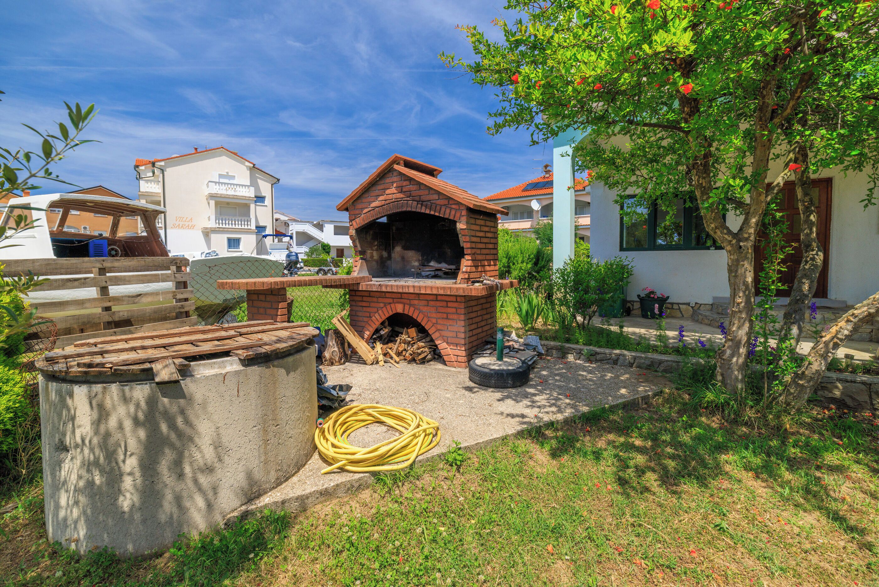 Lareira de tijolos ao ar livre, rodeada por um jardim com uma árvore e uma estrutura de concreto.