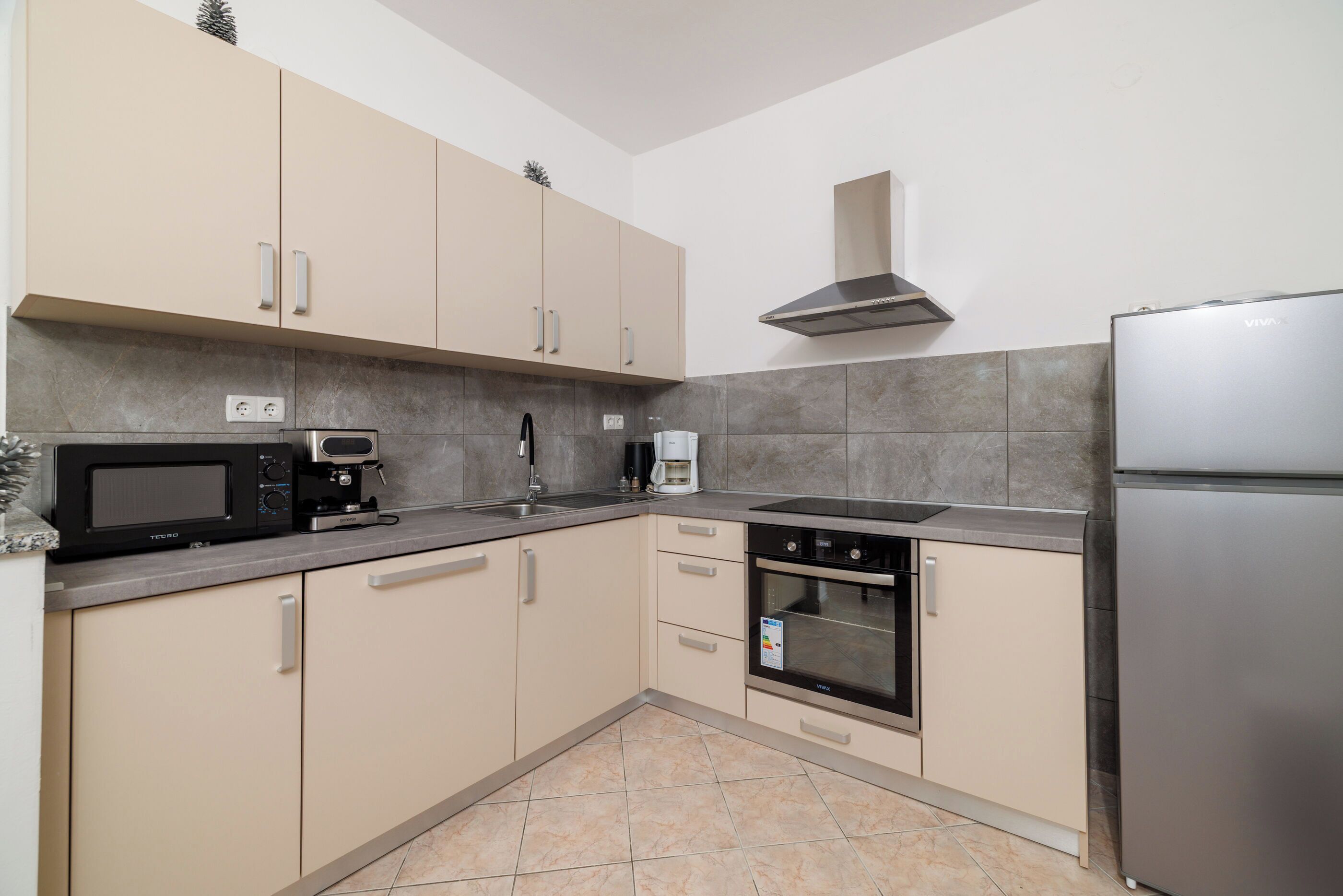 Una cocina moderna con armarios color beige, un refrigerador de acero inoxidable, un microondas, una cafetera y un horno.