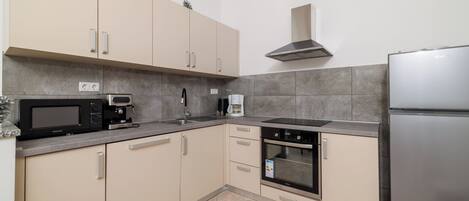 Una cocina moderna con armarios color beige, un refrigerador de acero inoxidable, un microondas, una cafetera y un horno.