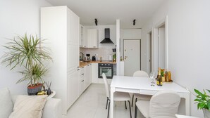 Una cucina compatta con mobili bianchi, una cappa aspirante nera e un'area pranzo con tavolo e sedie bianche.