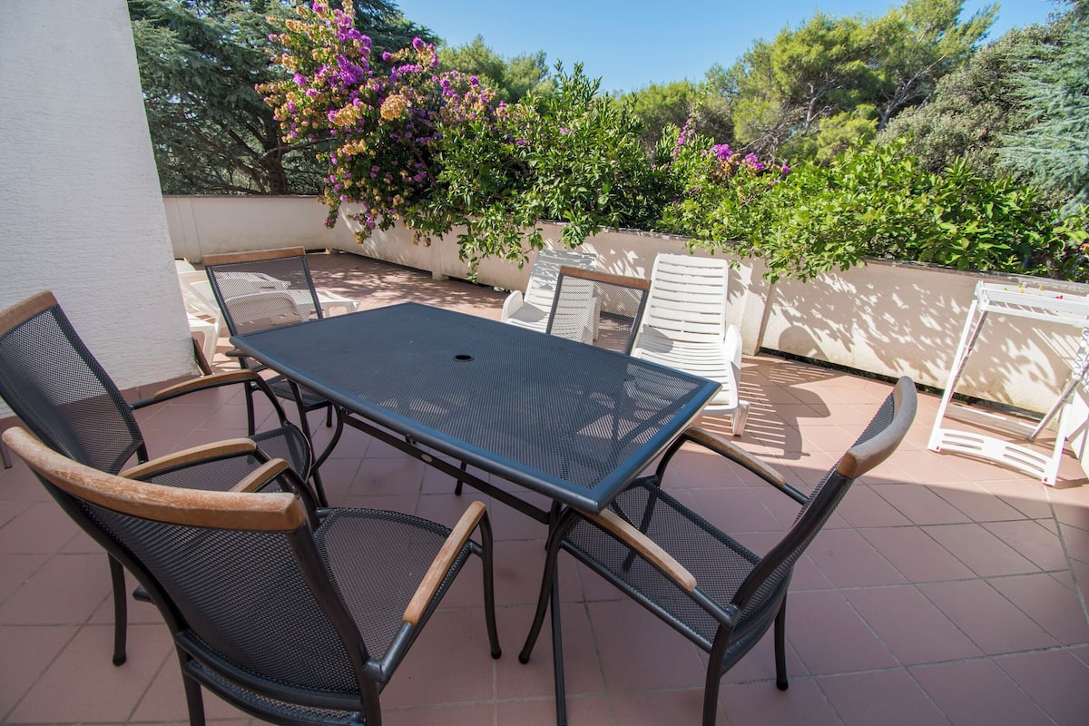 An outdoor patio with a table and chairs, surrounded by lush greenery and flowering plants.