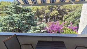 Un espace extérieur aménagé, abrité et doté d’une table et de chaises, qui offre une vue sur un jardin avec des arbres et des fleurs violettes.