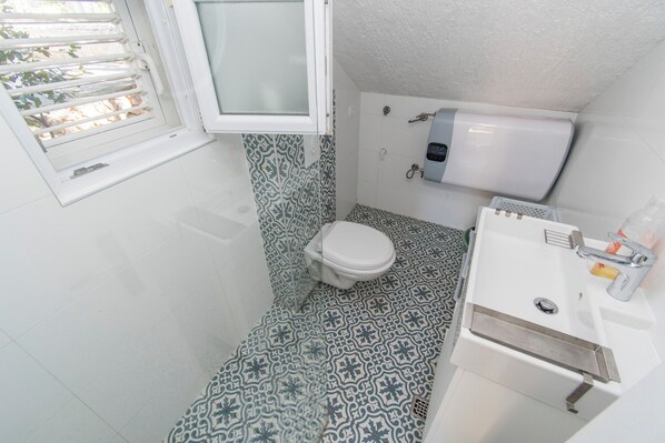 A small bathroom with a toilet, sink, and window. - Apartment Family Ribicic (Kolan)