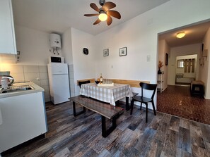 Una cucina funzionale con frigorifero, microonde e lavello. C'è un'area pranzo con tavolo e sedie, e una ventola a soffitto.