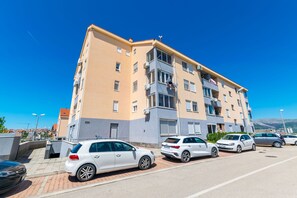 Ένα πολυώροφο κτίριο κατοικιών με μπαλκόνια, σταθμευμένα αυτοκίνητα και έναν καθαρό, γαλάζιο ουρανό.