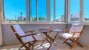 A room with two wooden chairs and a small table, large windows with a view of buildings and mountains, and a tiled floor. - Apartment Tino (Split)