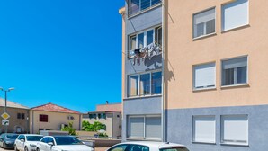 A multi-story building with a beige and gray facade, multiple windows, and a visible laundry line on the exterior. - Apartment Tino (Split)