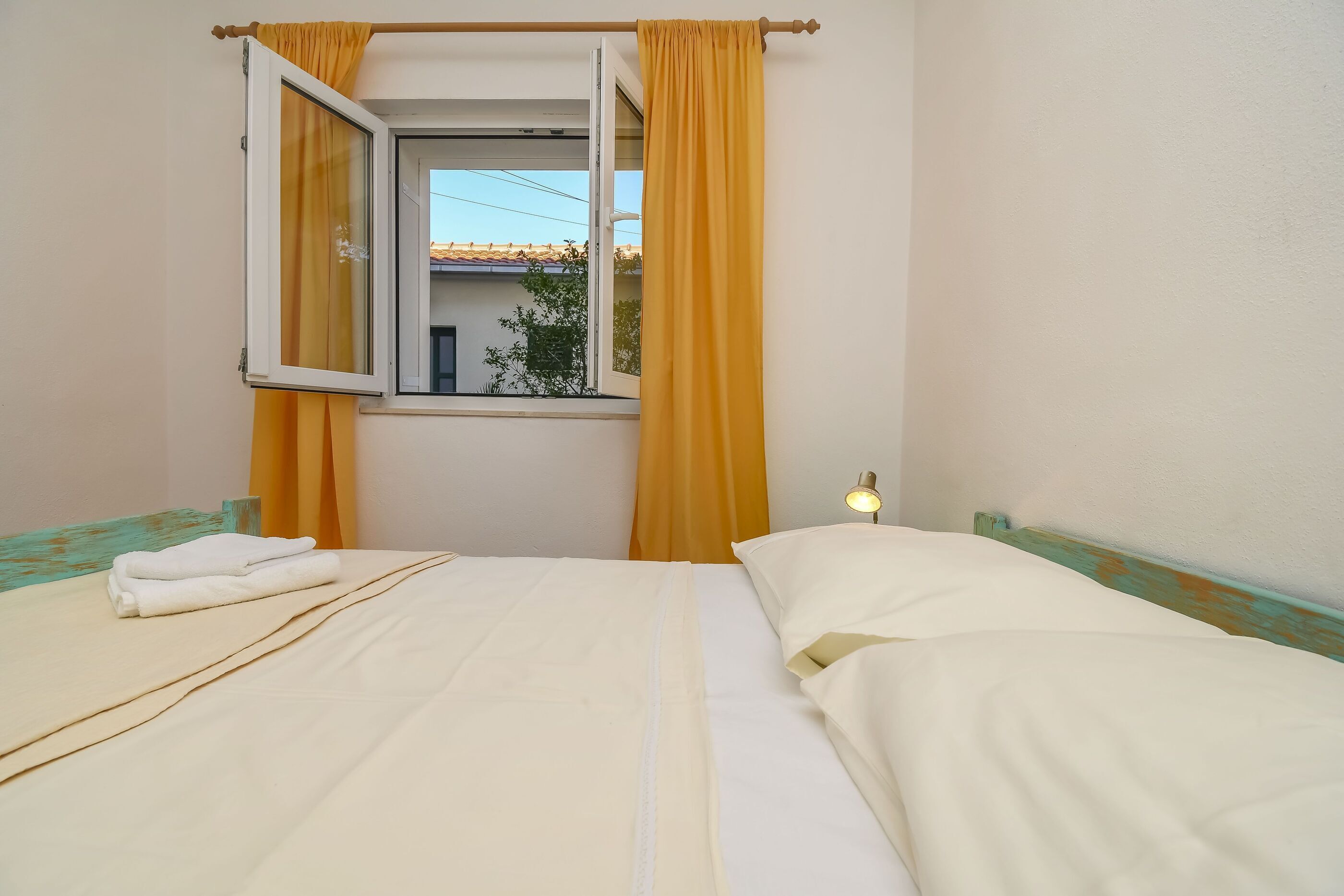 A room with a bed, a window with curtains, a bedside lamp, and a view of a building outside.