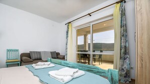 Een slaapkamer met een groot bed, een bank en een eethoek, zichtbaar door een schuifglazen deur.