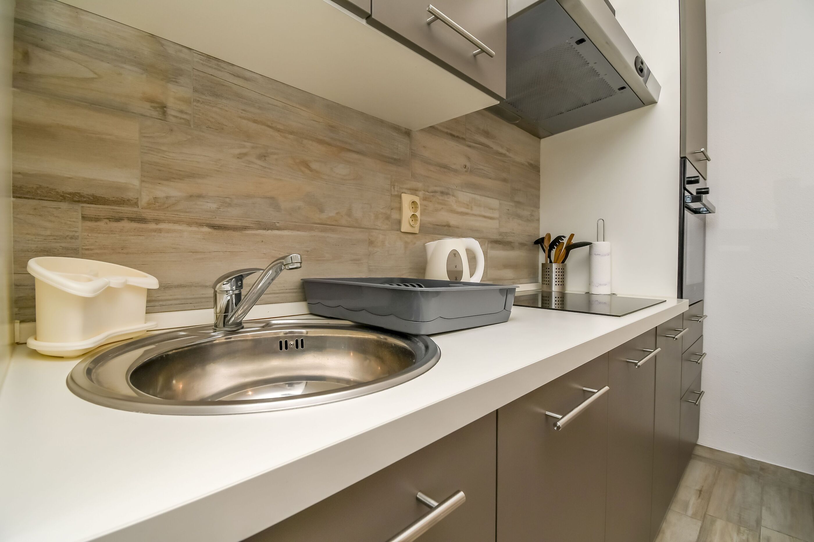 A modern kitchen with a stainless steel sink, a kettle, and a coffee maker on the counter.
