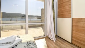 Een kamer met een grote schuifglazen deur die leidt naar een balkon met uitzicht op water en heuvels.