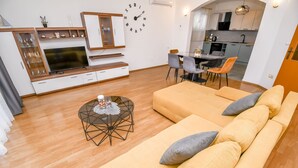 A modern living room with a large sofa, a TV, and a dining area with chairs and a table. - Apartments Smoljic (Trogir)