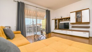 A modern living room with a yellow sofa, a TV, and a dining table. - Apartments Smoljic (Trogir)