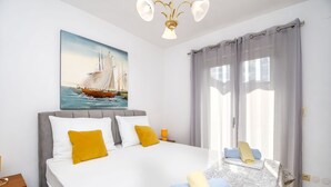 A neatly made bed with pillows, a bedside table with a lamp, and a painting of a sailboat on the wall. - Apartments Smoljic (Trogir)