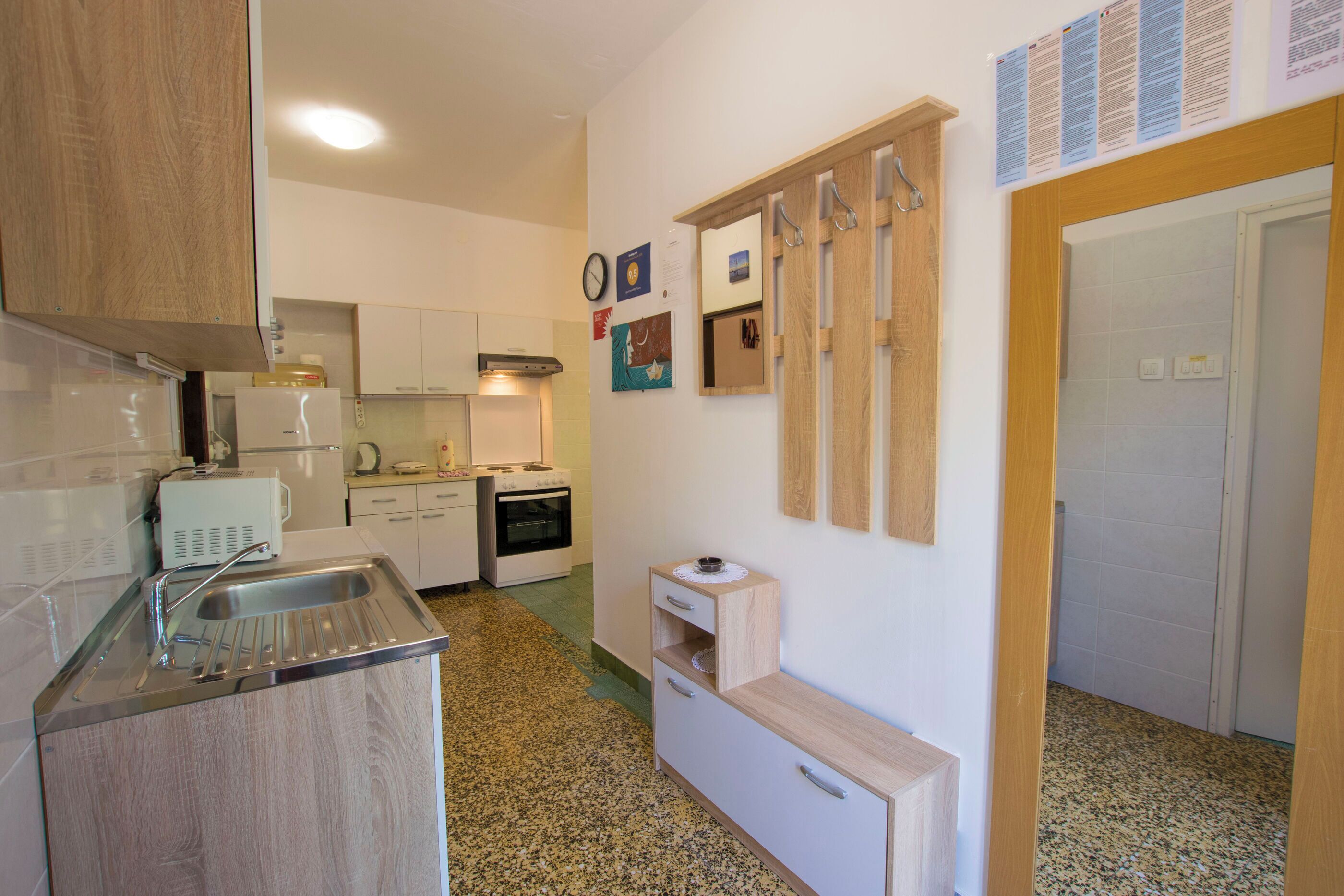 A compact kitchen with a sink, stove, and cabinets. There are wall-mounted hooks and a small cabinet with drawers.