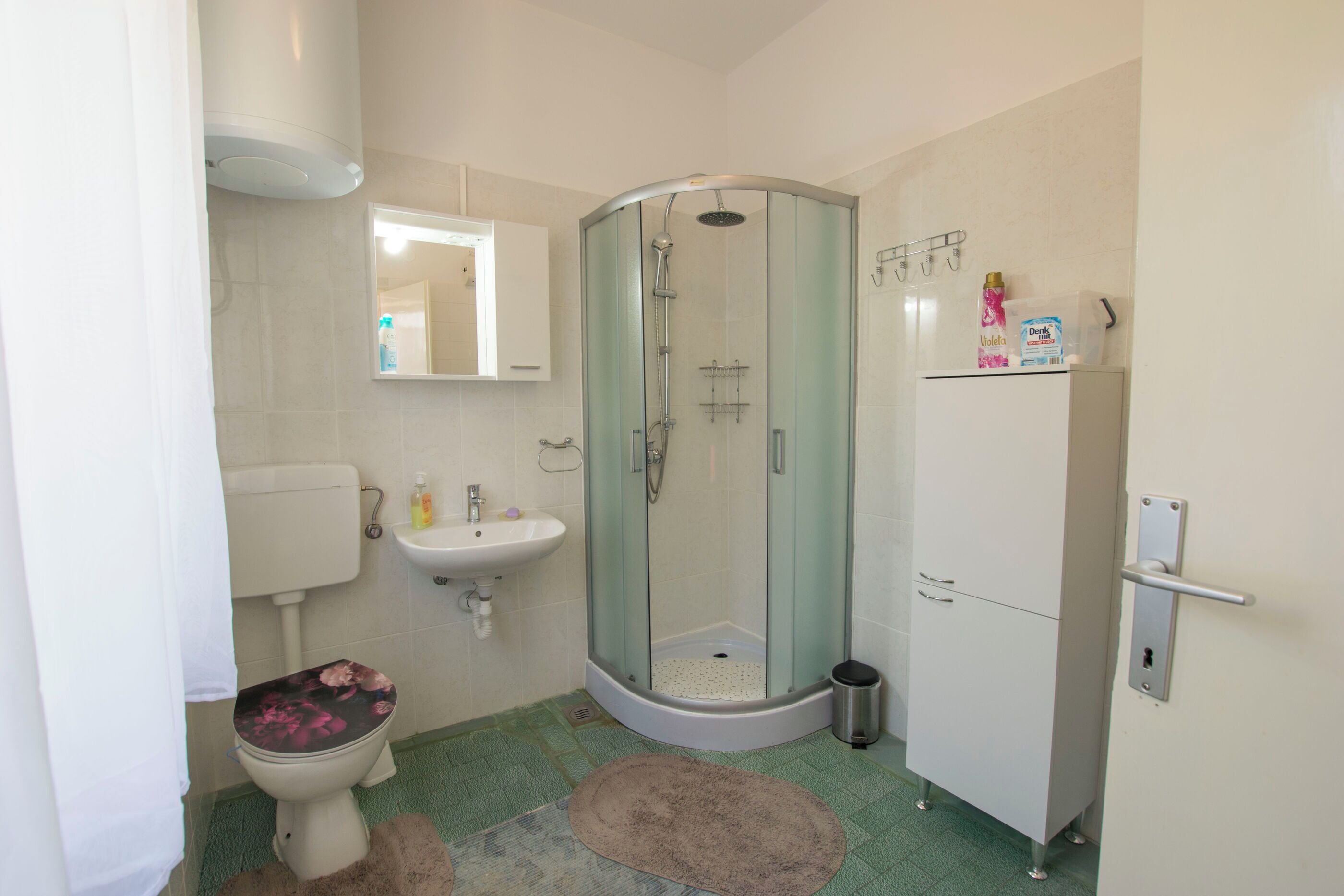 Un baño con inodoro, lavamanos, cabina de ducha de vidrio y un armario.