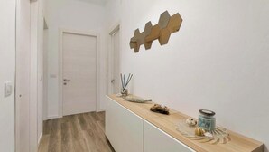Een gang met een houten vloer, een witte deur en een lange houten bank met decoratieve objecten.