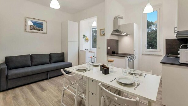 Een moderne keuken met witte kasten, een inbouwfornuis en een eethoek met een witte tafel en stoelen.