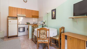 Una cucina compatta con mobili in legno, un frigorifero, un forno e una lavatrice. C'è un tavolo da pranzo con sedie e una TV a schermo piatto montata a parete.