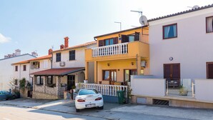 Una fila di edifici residenziali con balconi, un'auto parcheggiata davanti e cielo sereno.