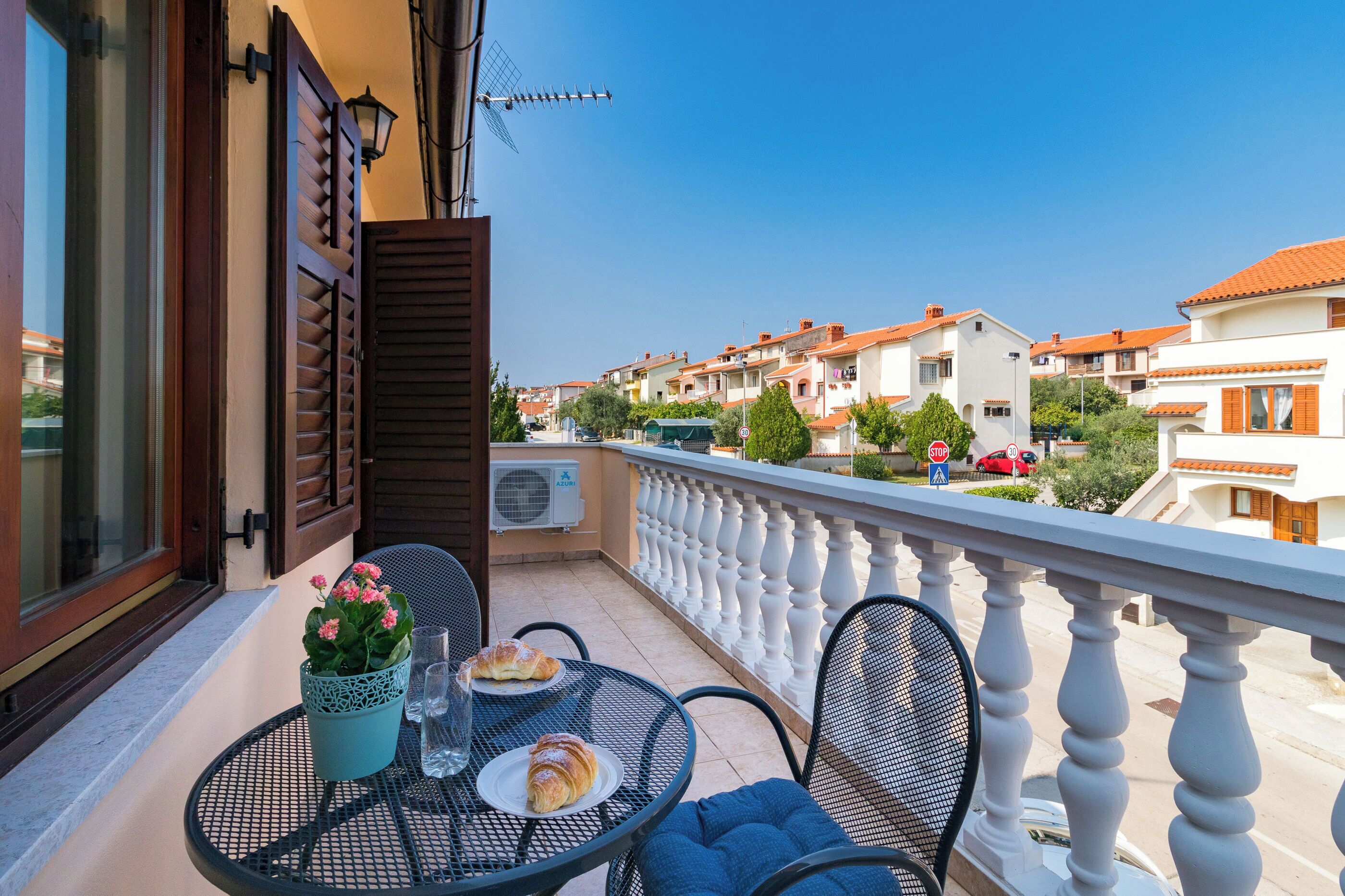 A balcony with a table, chairs, a potted plant, and a plate with food.