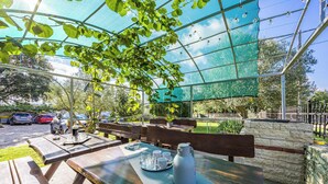 Un café en plein air avec des tables et des bancs en bois, une serre en verre et un mur de pierre en arrière-plan.