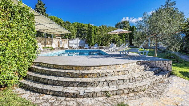 Une piscine en pierre, accessible par des marches, entourée de verdure et dotée d’un espace abrité.