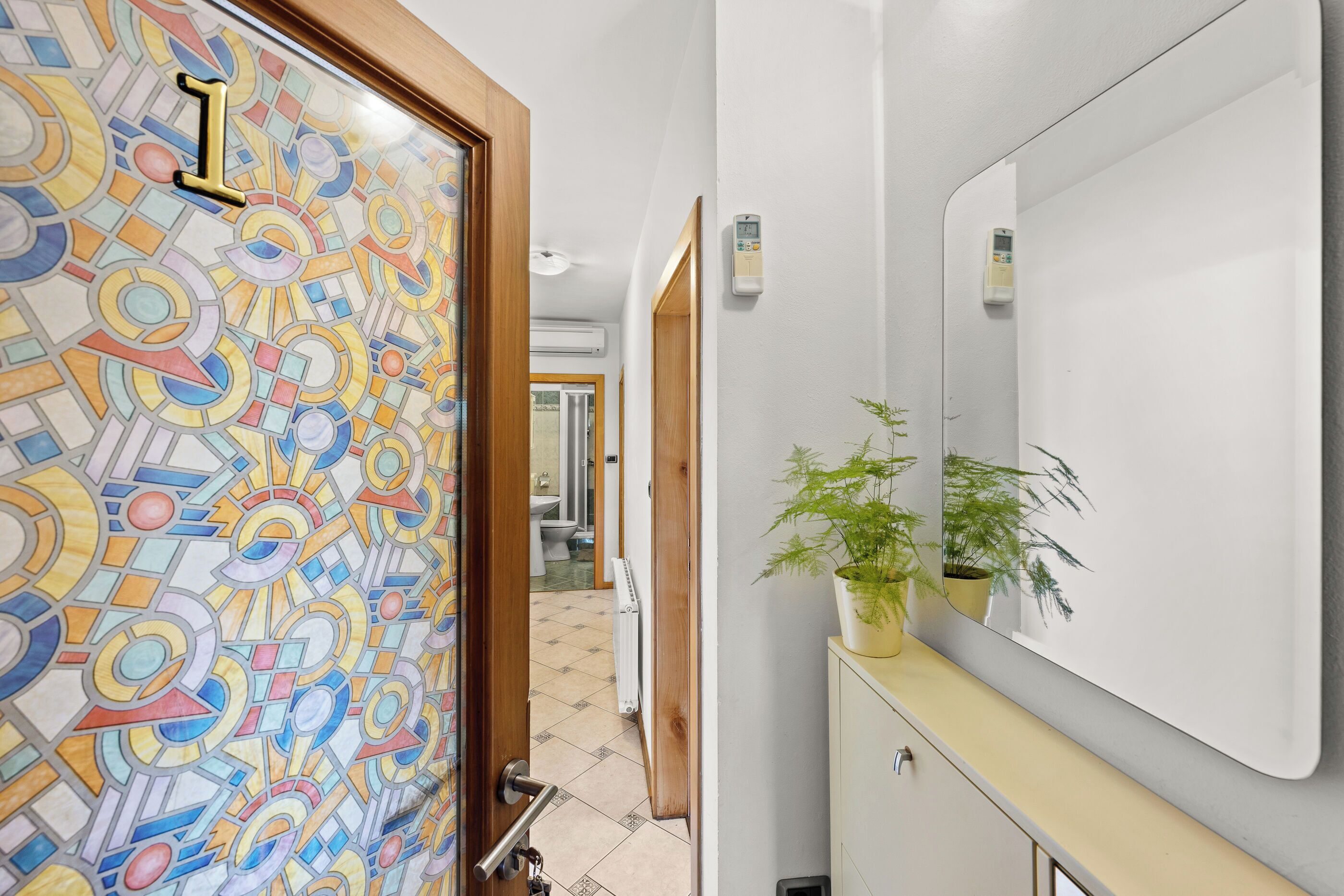 A bathroom with a colorful mosaic wall, a potted plant, a mirror, and a door with a number.