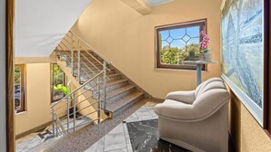 Un intérieur moderne avec un escalier, un fauteuil confortable et une grande fenêtre donnant sur un paysage verdoyant.