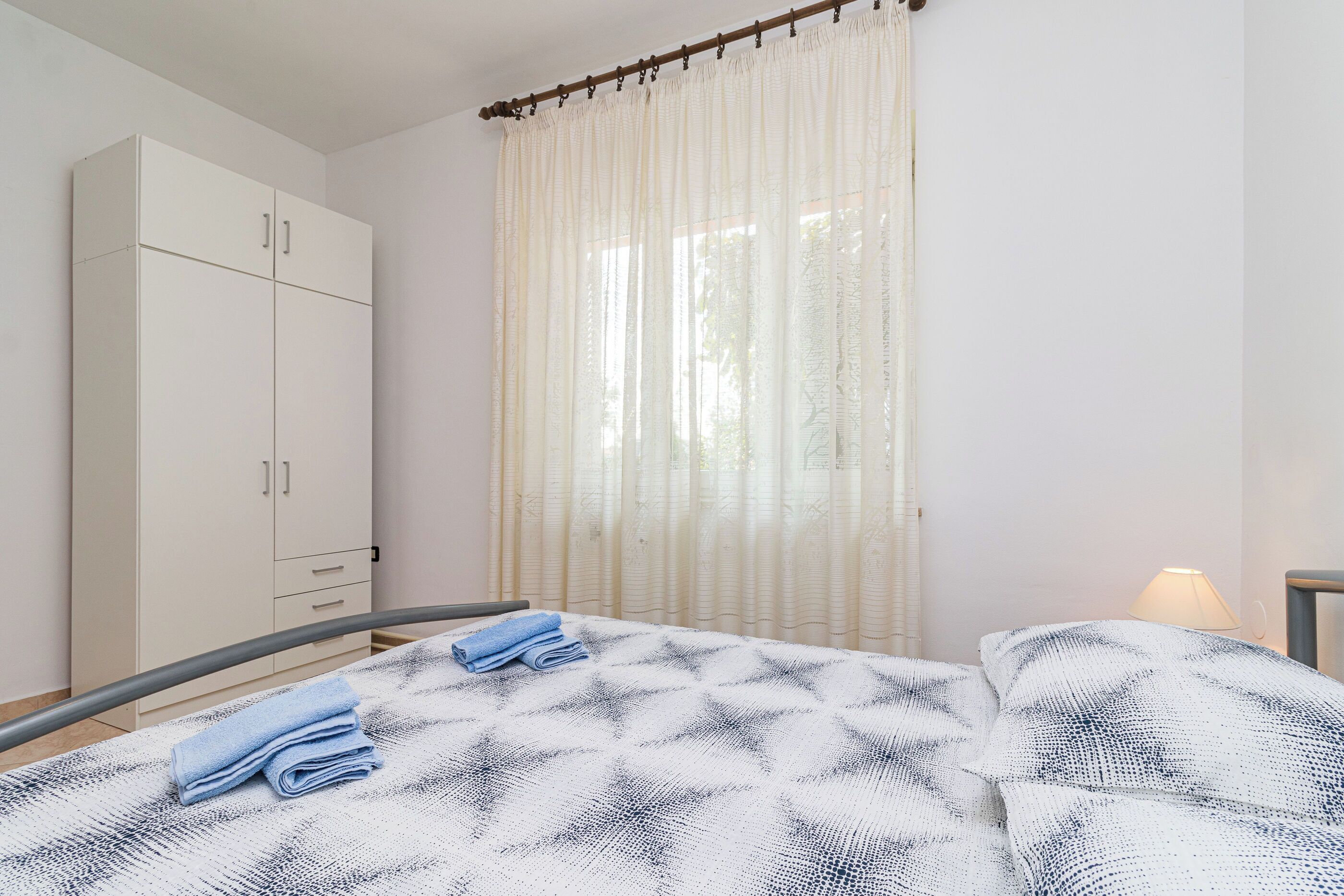 A bedroom with a bed, a wardrobe, and a window with curtains.