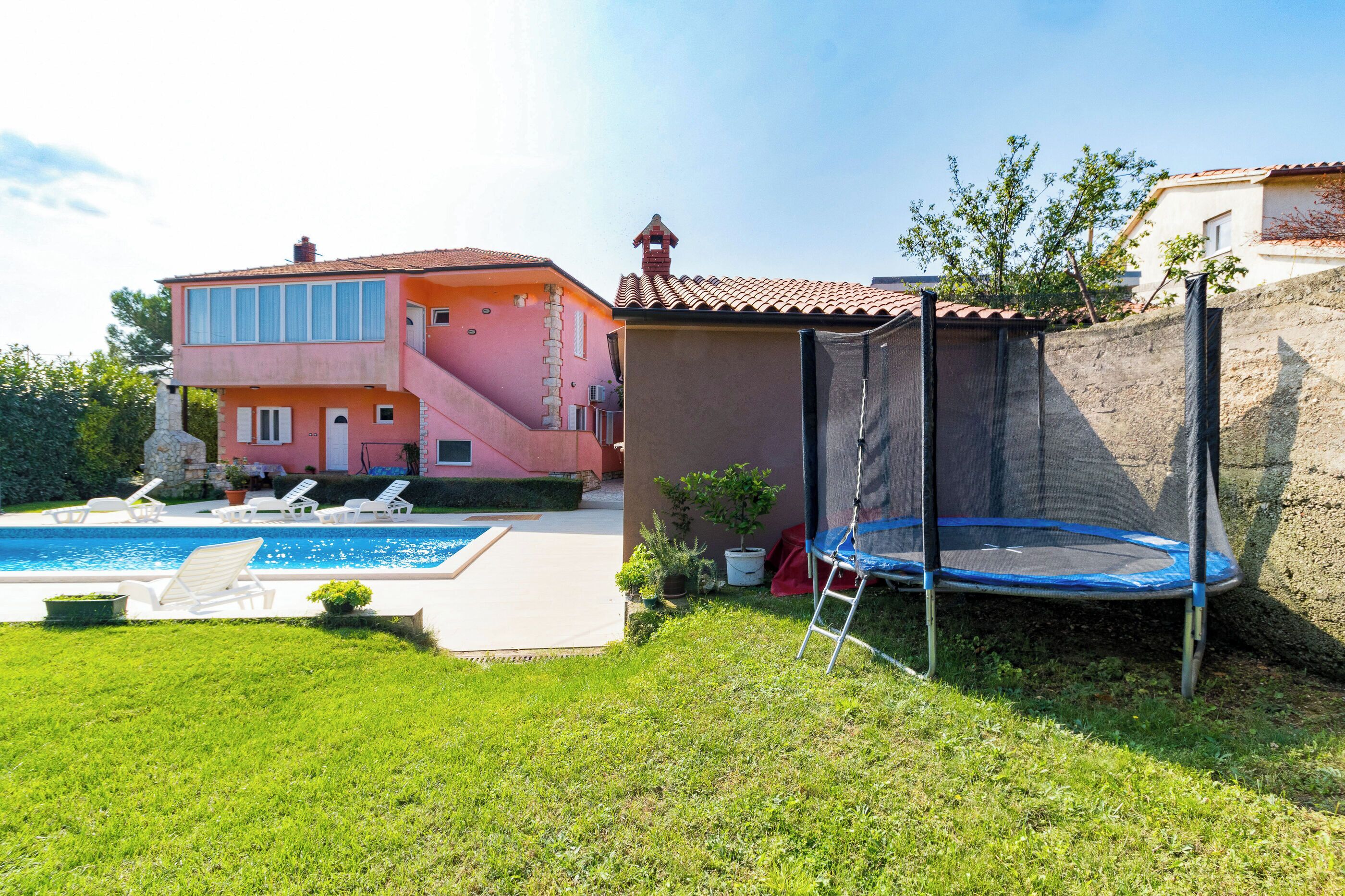 A two-story house with a swimming pool, a trampoline, and a garden.