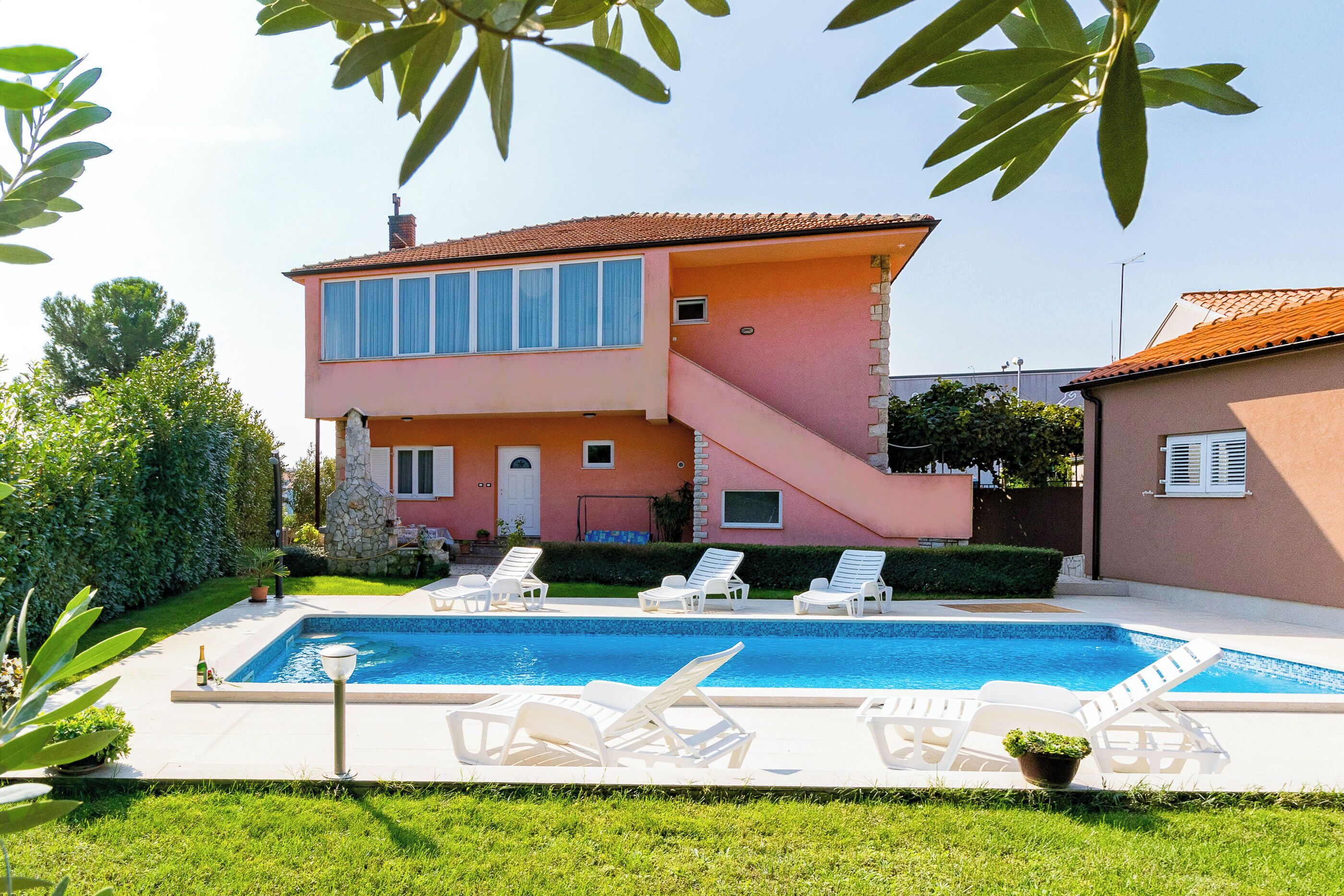 A two-story house with a swimming pool, outdoor seating, and a staircase leading to the upper floor.