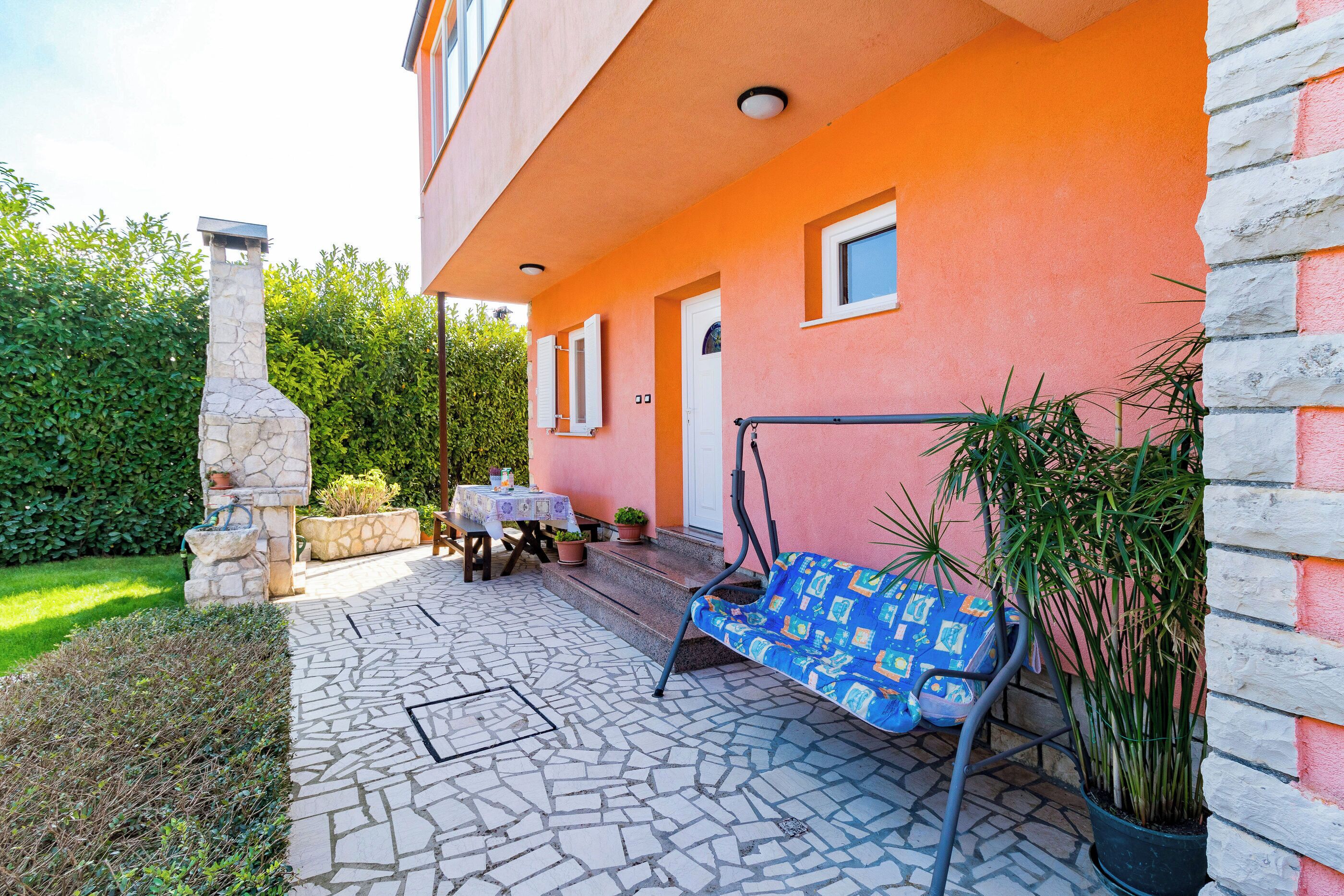 A patio with a stone floor, a swing chair, a table with chairs, and a potted plant.
