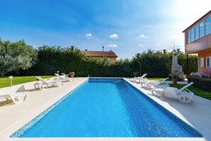 Ein rechteckiger Pool mit einer gefliesten Kante, umgeben von weißen Liegestühlen und einer Steinfountain.