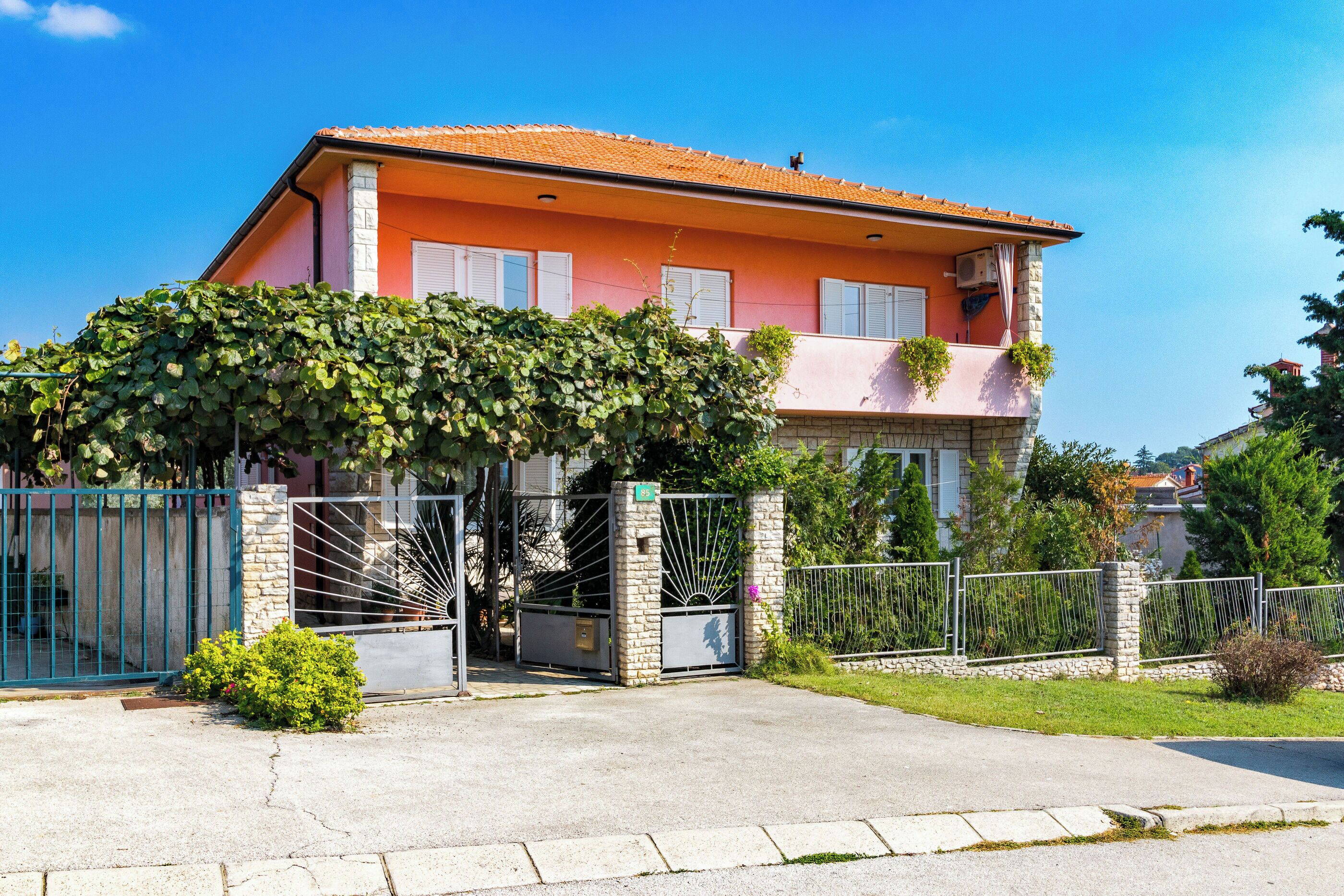 A two-story house with a stone facade, a tiled roof, and a gated entrance.