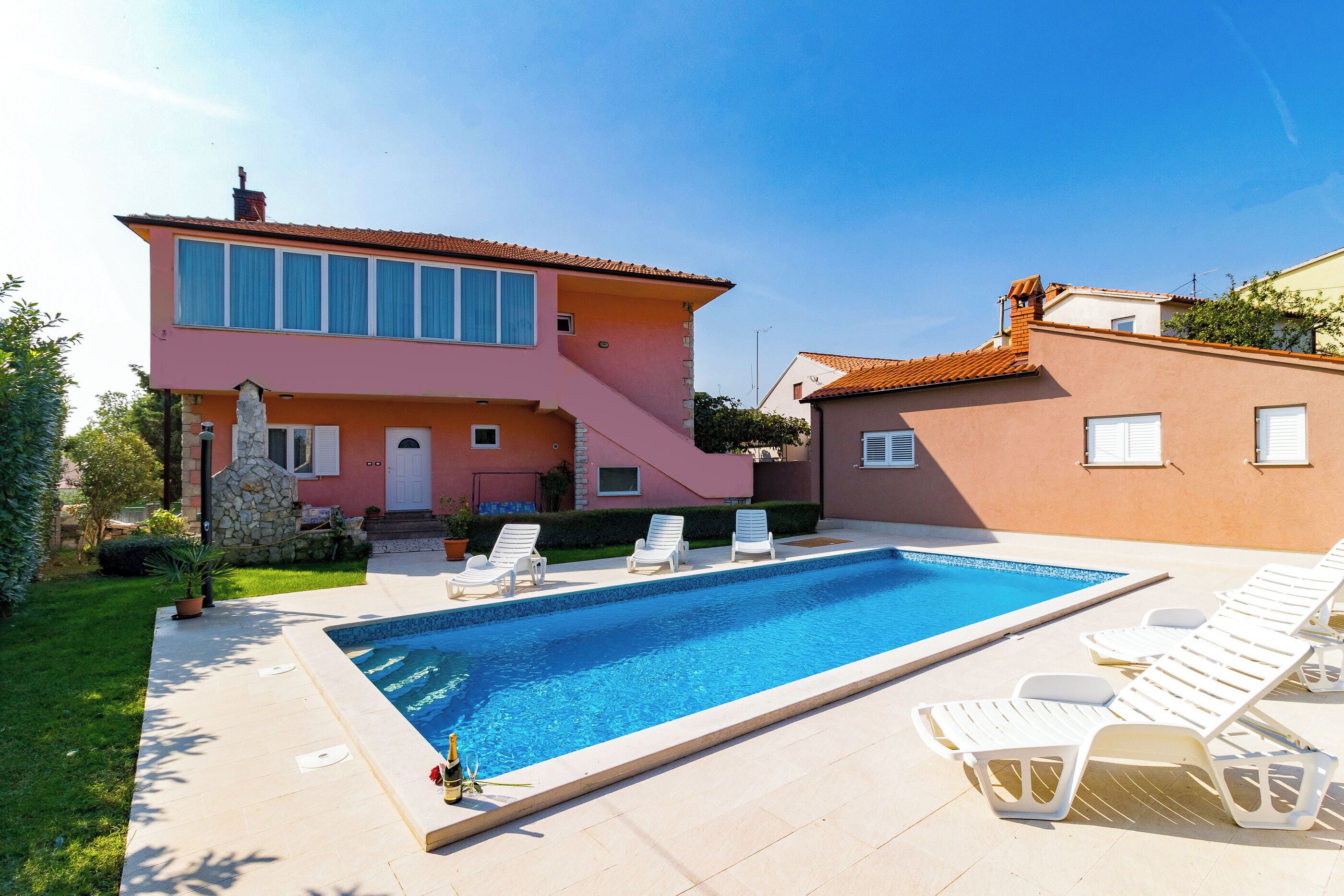 Une maison à deux étages avec une piscine et des chaises longues.
