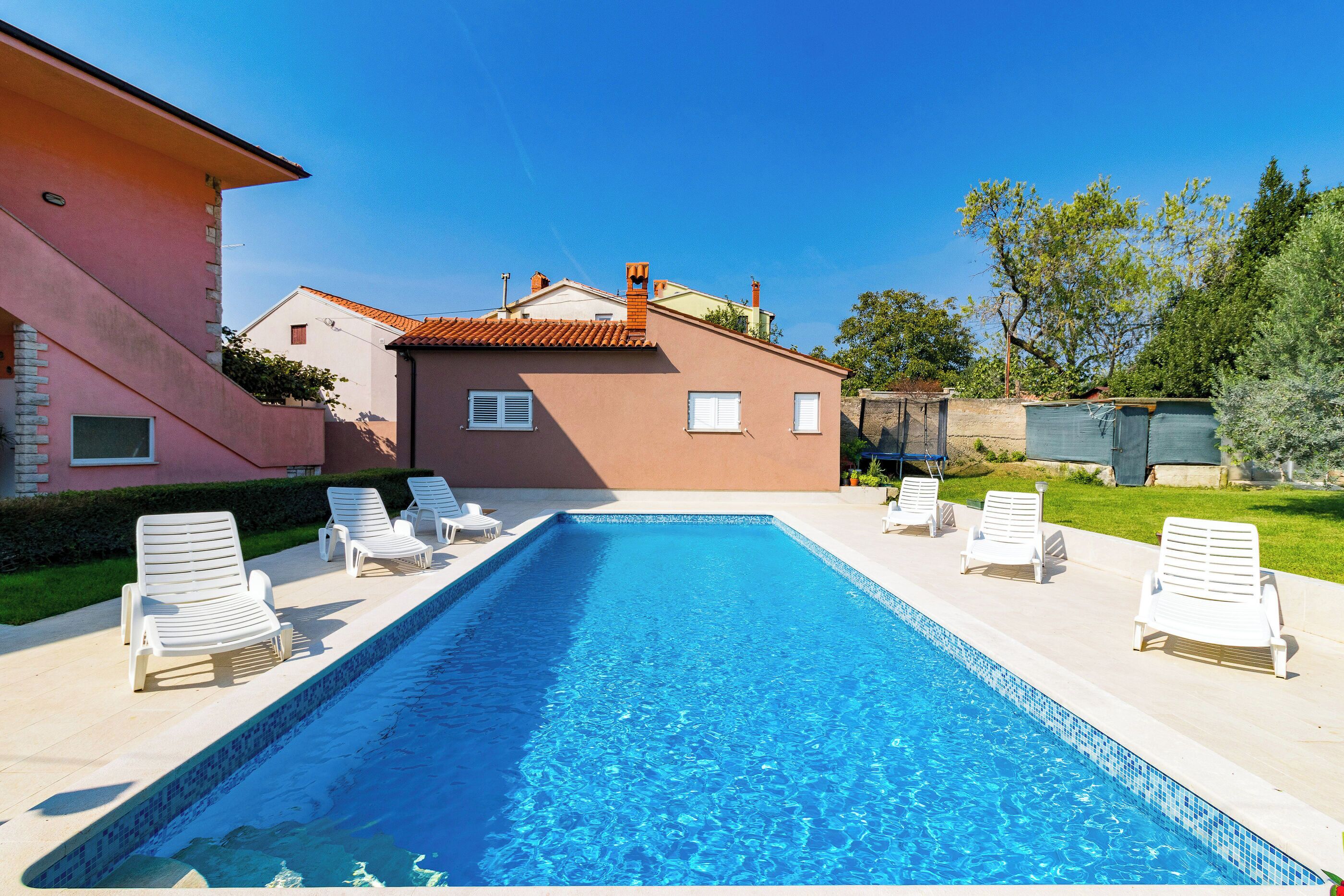 A rectangular swimming pool with clear blue water, surrounded by white lounge chairs.