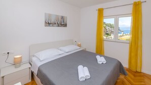 A bedroom with a bed, a nightstand, a lamp, and a painting of sailboats. - House Mateljan (Jelsa)