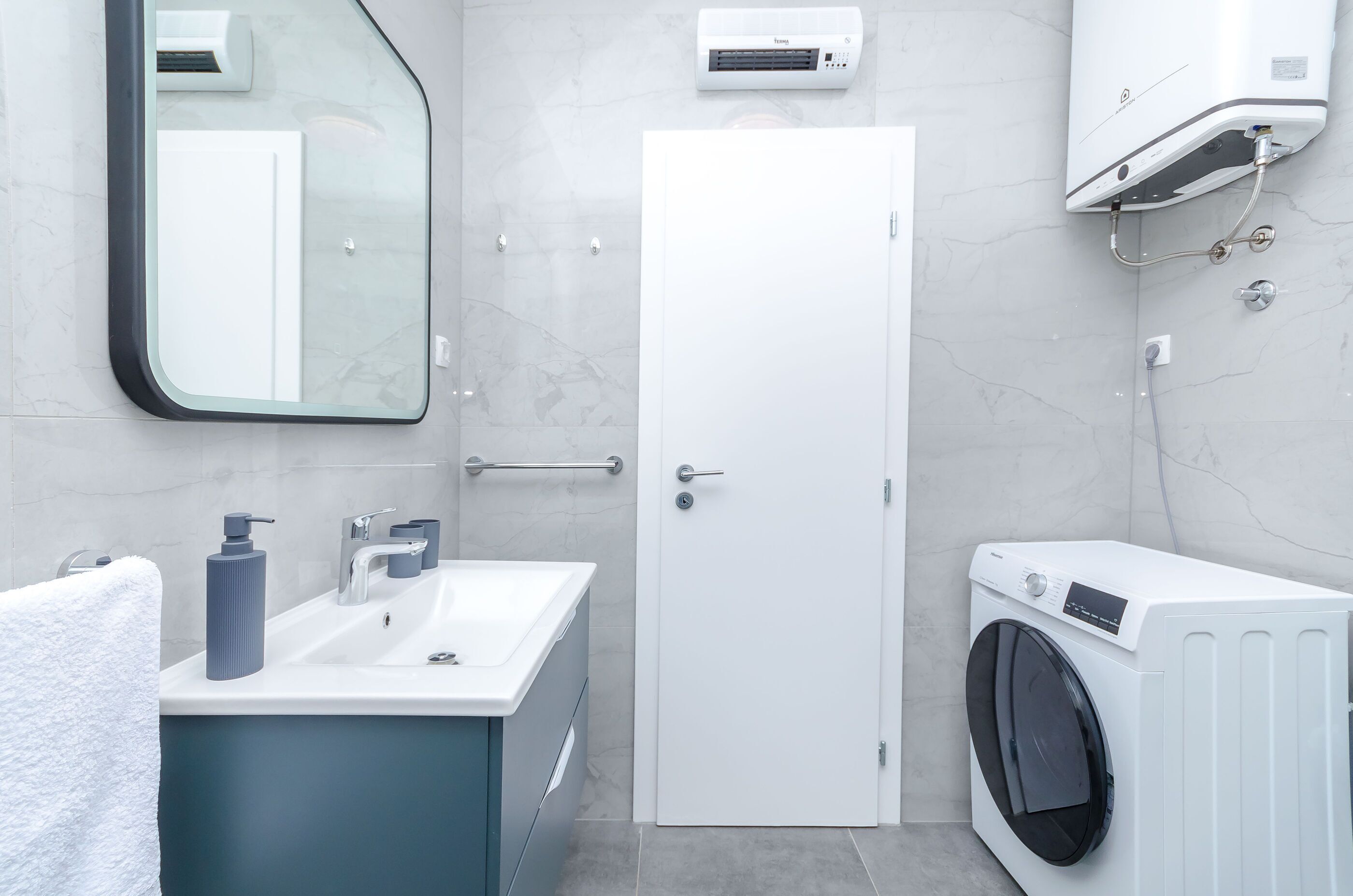 A modern bathroom with a sink, mirror, towel rack, and a washing machine.