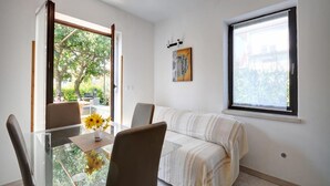Um espaço de estar compacto com uma mesa de jantar de vidro, um sofá e uma janela grande que oferece vista para o verde lá fora.