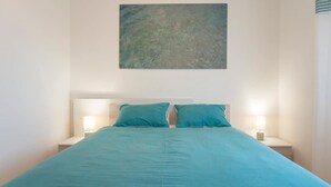 Quarto com cama, duas mesas de cabeceira e uma obra de arte na parede.