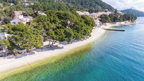 A coastal area with a beach, clear water, and residential buildings. - Apartments Kovami (Podgora)