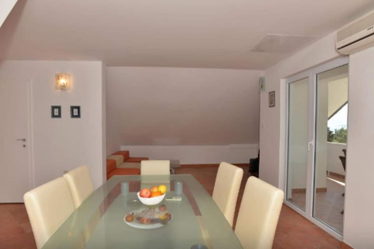 Un coin repas avec une table en verre, quatre chaises et un saladier rempli de fruits.