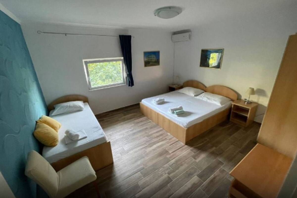 Une chambre avec deux lits, un bureau, une chaise, une fenêtre et un ventilateur de plafond.